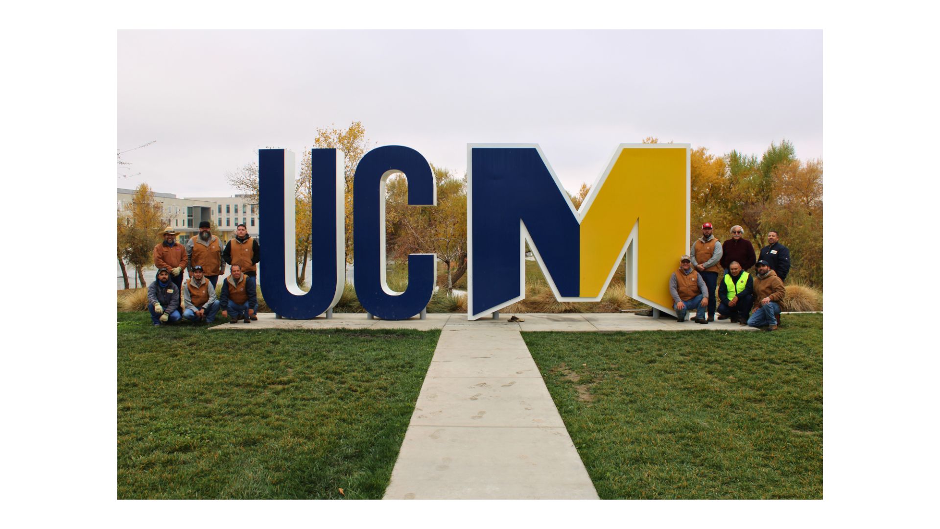 Picture of Grounds Crew in front of blue and gold UCM logo sign